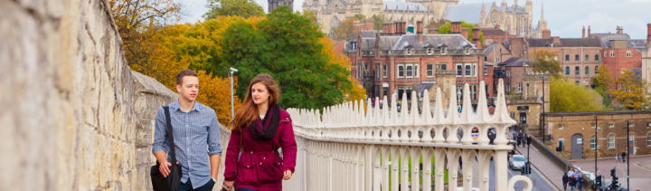 Two students walking along the York City Walls talking with one another.